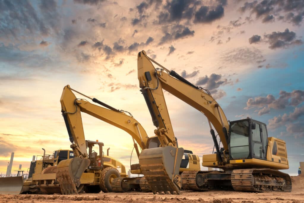 Construction equipment in a dirt lot with the sunsetting